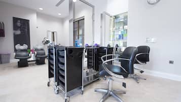 A modern salon with a clean, minimalist design, featuring a large mirror, black salon chairs, and a cart with various hair products.