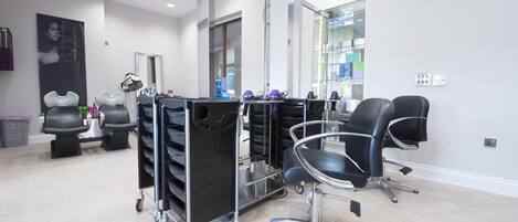 A modern salon with a clean, minimalist design, featuring a large mirror, black salon chairs, and a cart with various hair products.