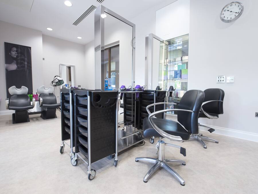 A modern salon with a clean, minimalist design, featuring a large mirror, black salon chairs, and a cart with various hair products.