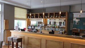 Una zona de bar con mostradores de madera, taburetes y una gran variedad de botellas y vasos.