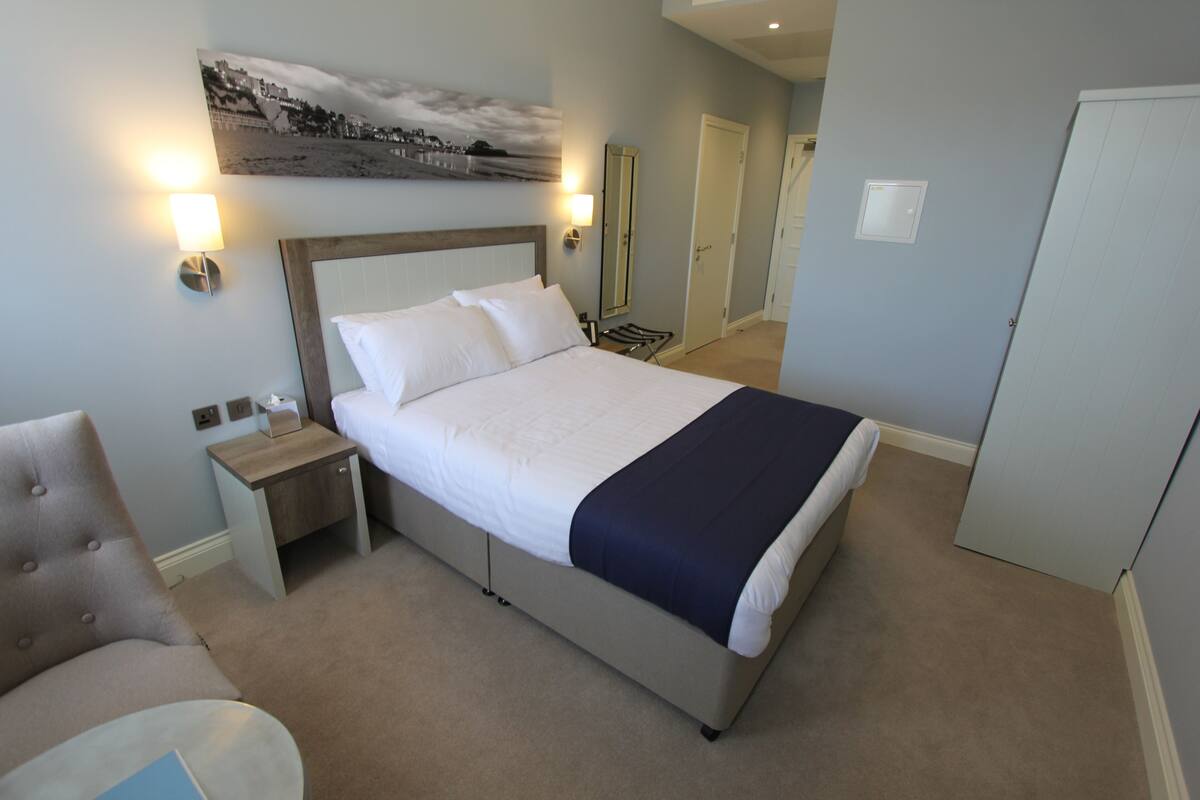 A neatly arranged hotel room with a large bed, bedside tables, a chair, and a wall-mounted artwork.