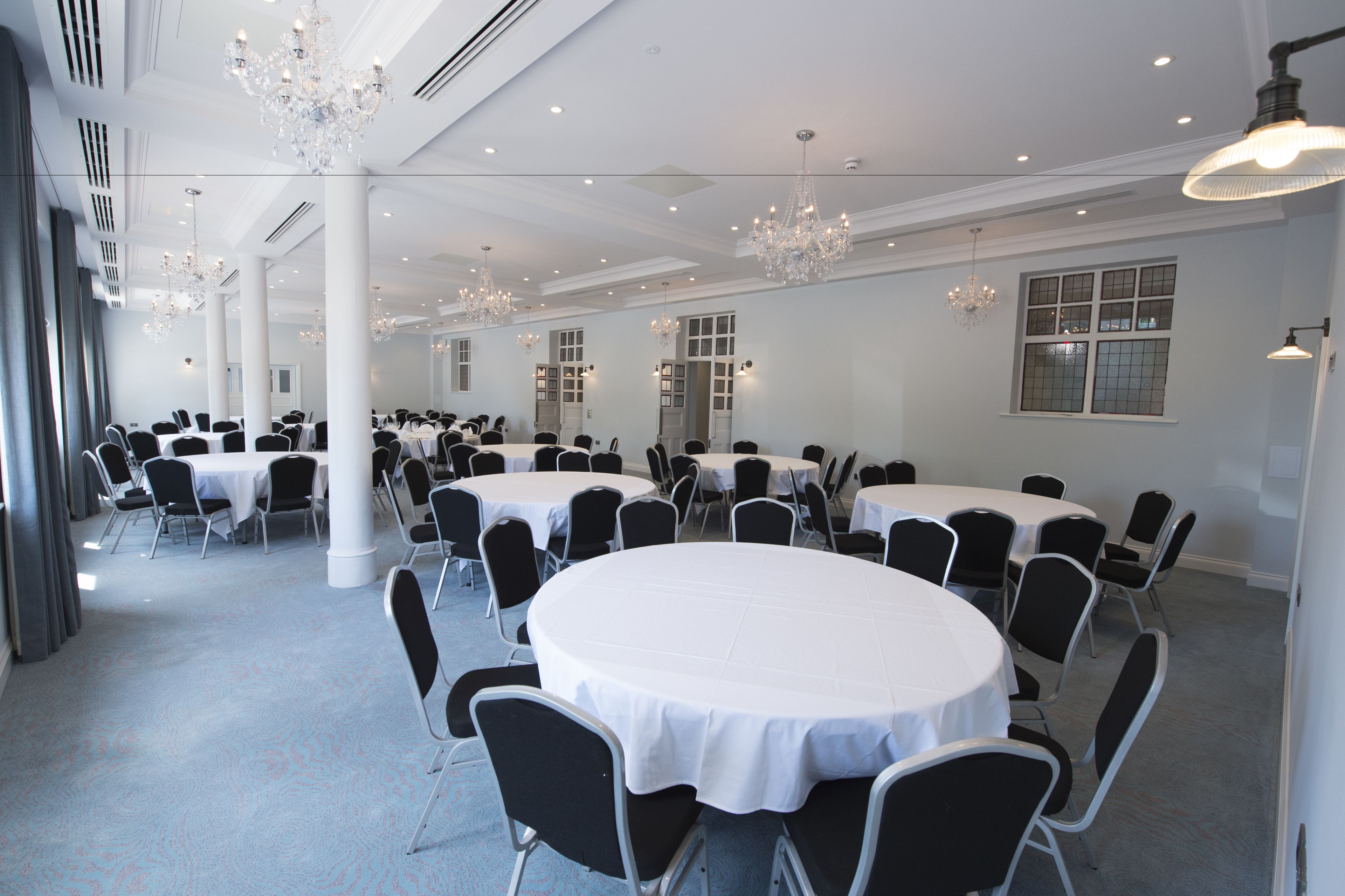 Un gran salón de banquetes con mesas redondas y sillas negras, paredes blancas y candelabros.