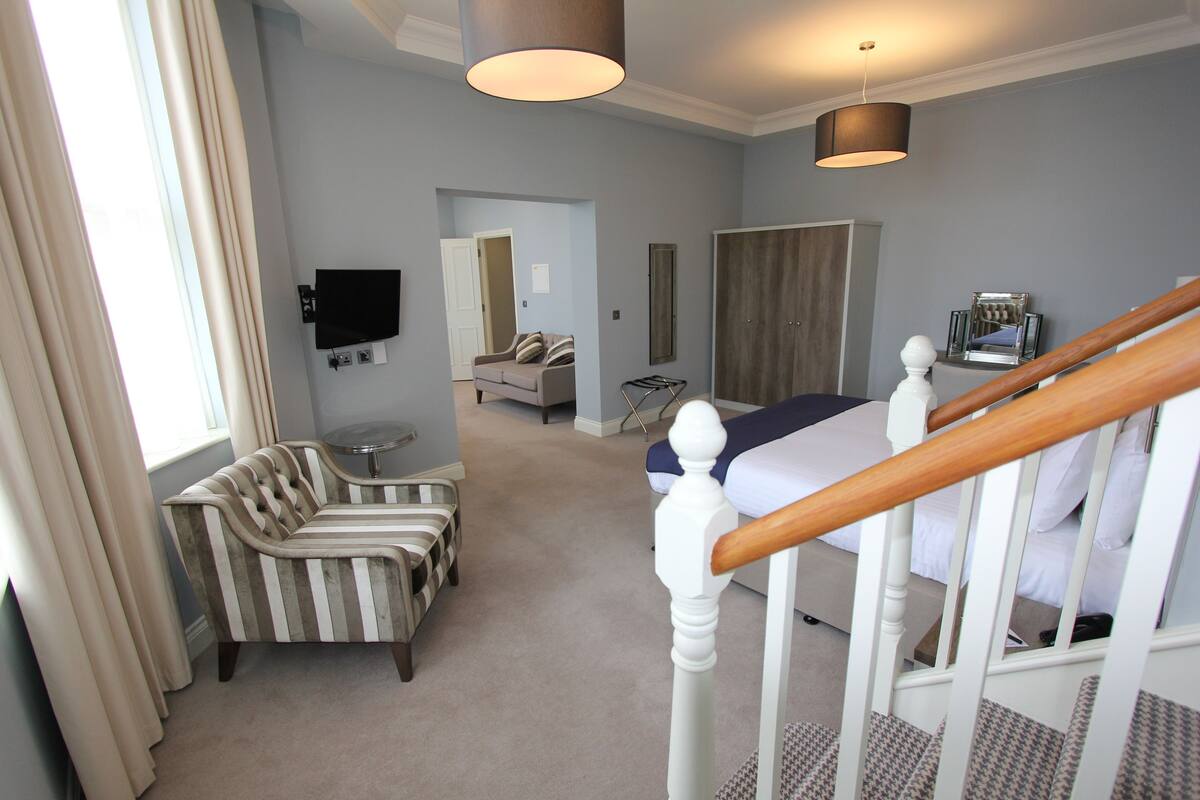 A hotel room with a bed, a sofa, a TV, and a staircase.