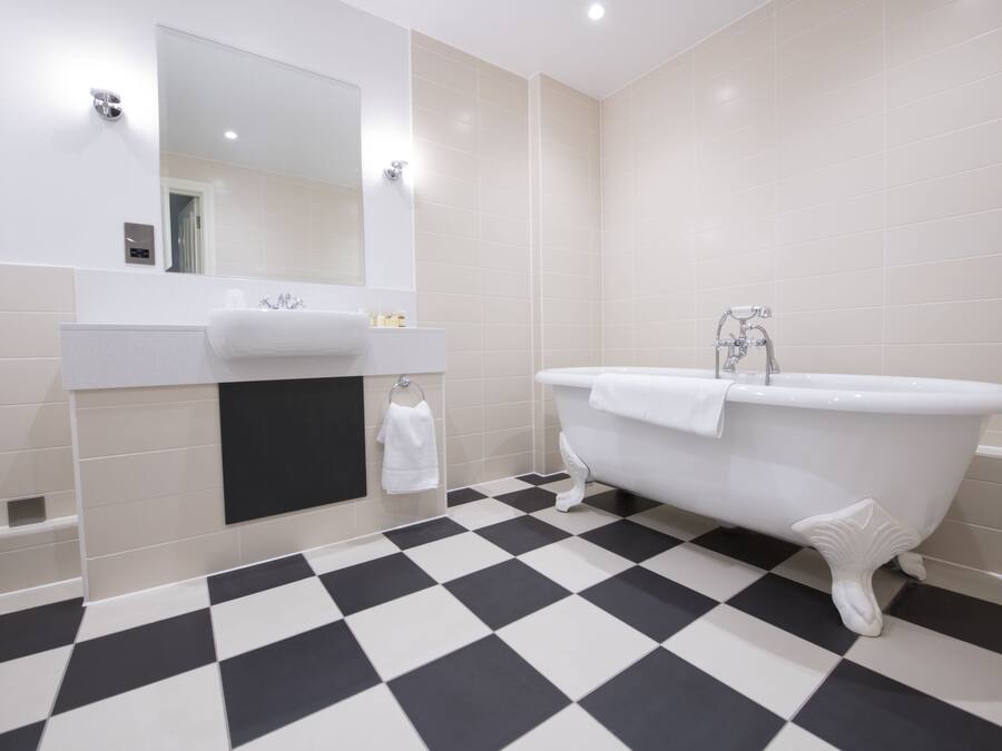 A bathroom with a checkered floor, a white bathtub, and a mirror above the sink.