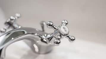 A close-up of a silver faucet with a cross-shaped handle and a circular knob, likely part of a bathroom fixture.