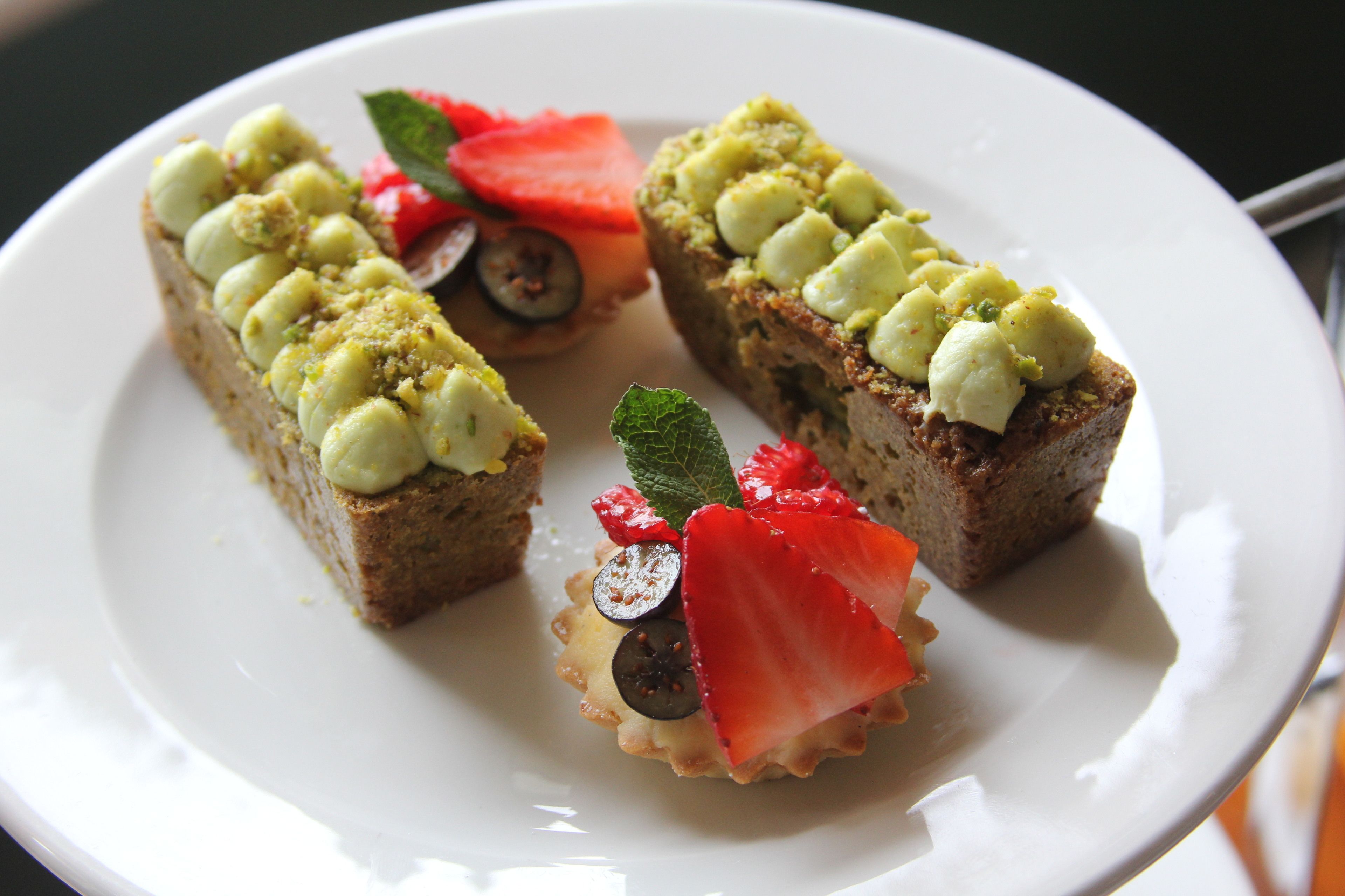 A plate with three pieces of pastry topped with green cream and strawberries.