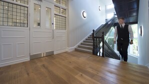 Una habitación amplia con suelo de madera, una escalera con barandilla negra y ventanas grandes con diseño de cuadrícula.