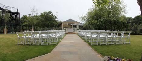 A stone pathway leading to a gazebo with white chairs arranged on either side.