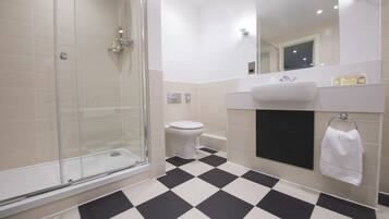 A bathroom with a checkered floor, a glass shower enclosure, a toilet, a sink, and a mirror.