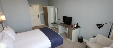 Una habitación de hotel con cama, escritorio, televisor, silla y lámpara.