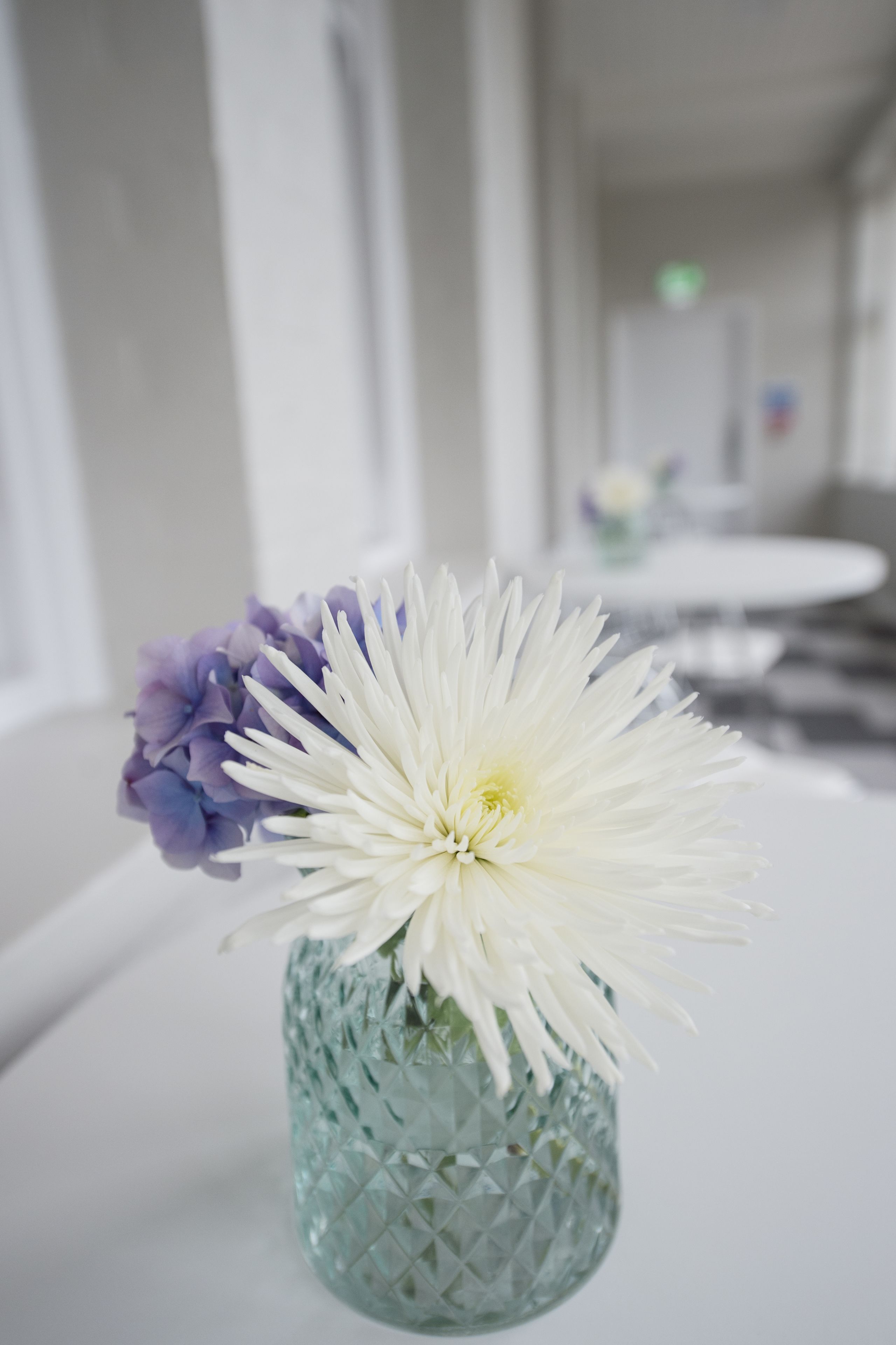 Un jarrón con flores blancas y moradas sobre una mesa blanca en una habitación de hotel.