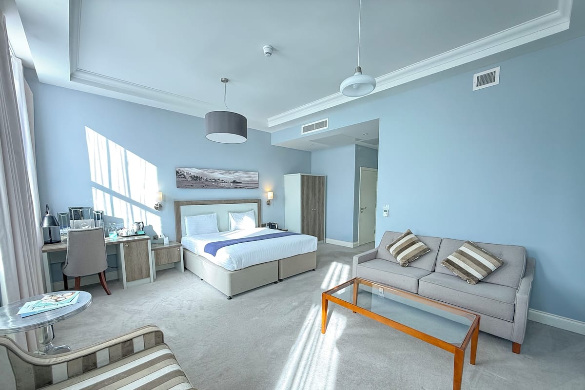 A modern hotel room with a large bed, a sofa, a desk, and a coffee table.