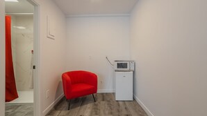 Une petite pièce étroite, avec une chaise rouge, un four à micro-ondes blanc et une porte qui donne sur une autre pièce.