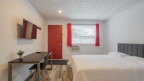 Une chambre moderne comprenant un lit, un bureau, une chaise, un téléviseur et une fenêtre avec des rideaux.