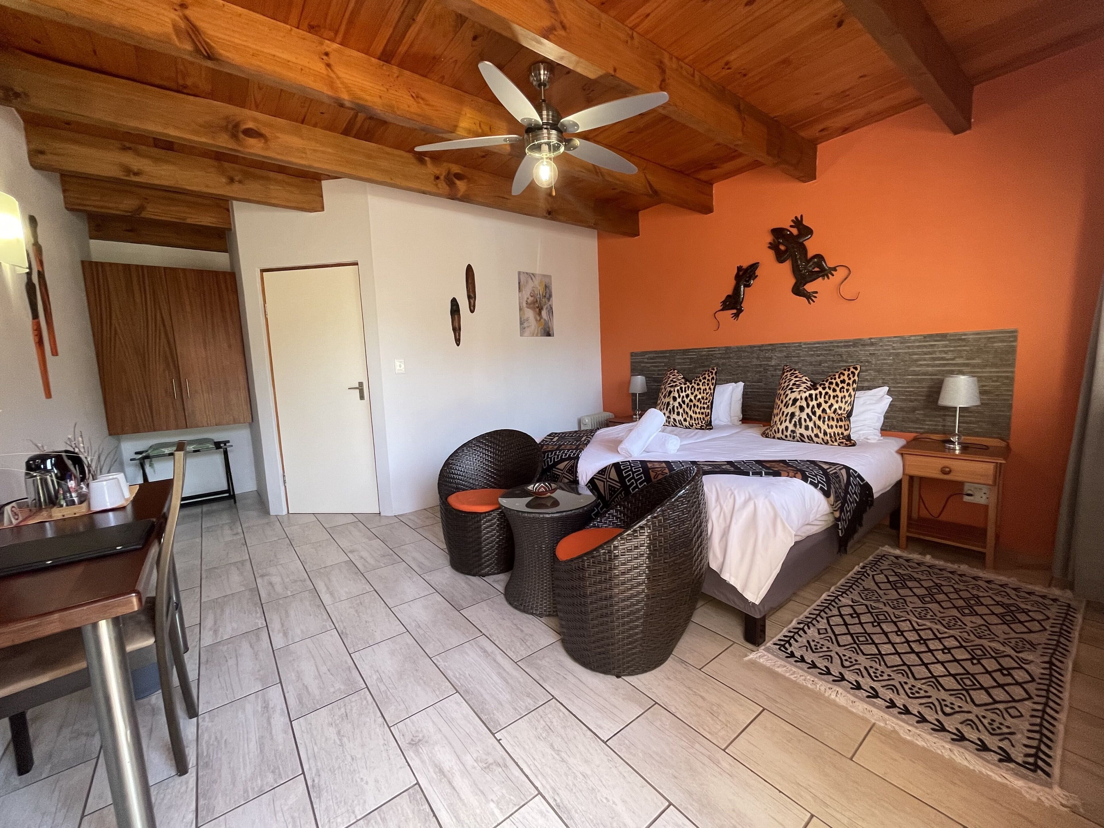 Une chambre à coucher comprenant un lit, un ventilateur de plafond, une table de chevet, une lampe, une chaise, une table et une porte.
