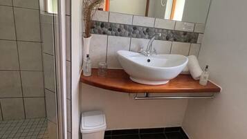 Une salle de bain avec un lavabo blanc, un miroir, une petite poubelle et un tapis de bain jaune.