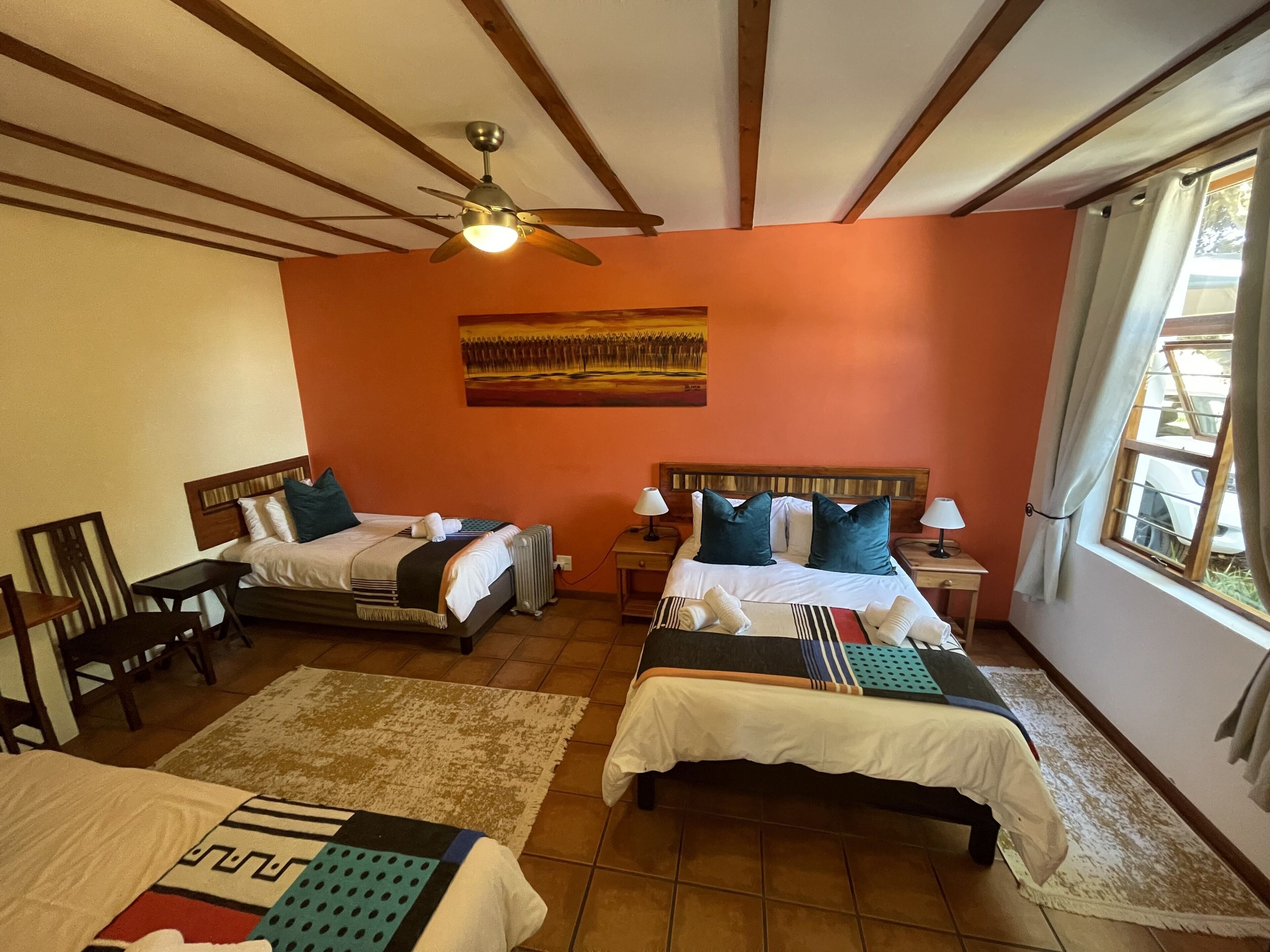 A hotel room with two beds, a ceiling fan, a painting on the wall, and a window with curtains.