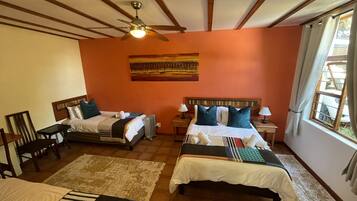 A hotel room with two beds, a ceiling fan, a painting on the wall, and a window with curtains.