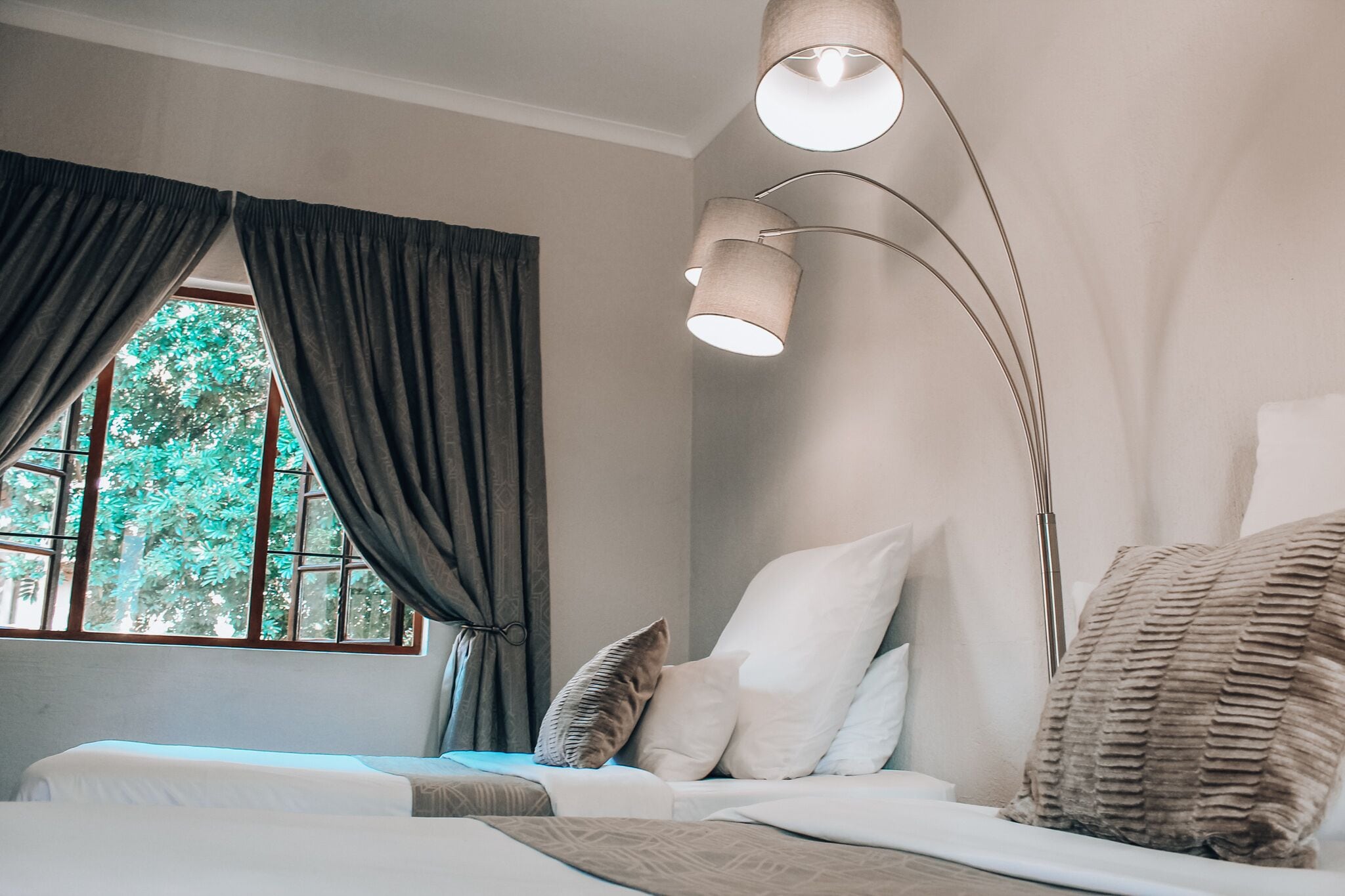 Un dormitorio con cama, una ventana con cortinas y una lámpara de pie.