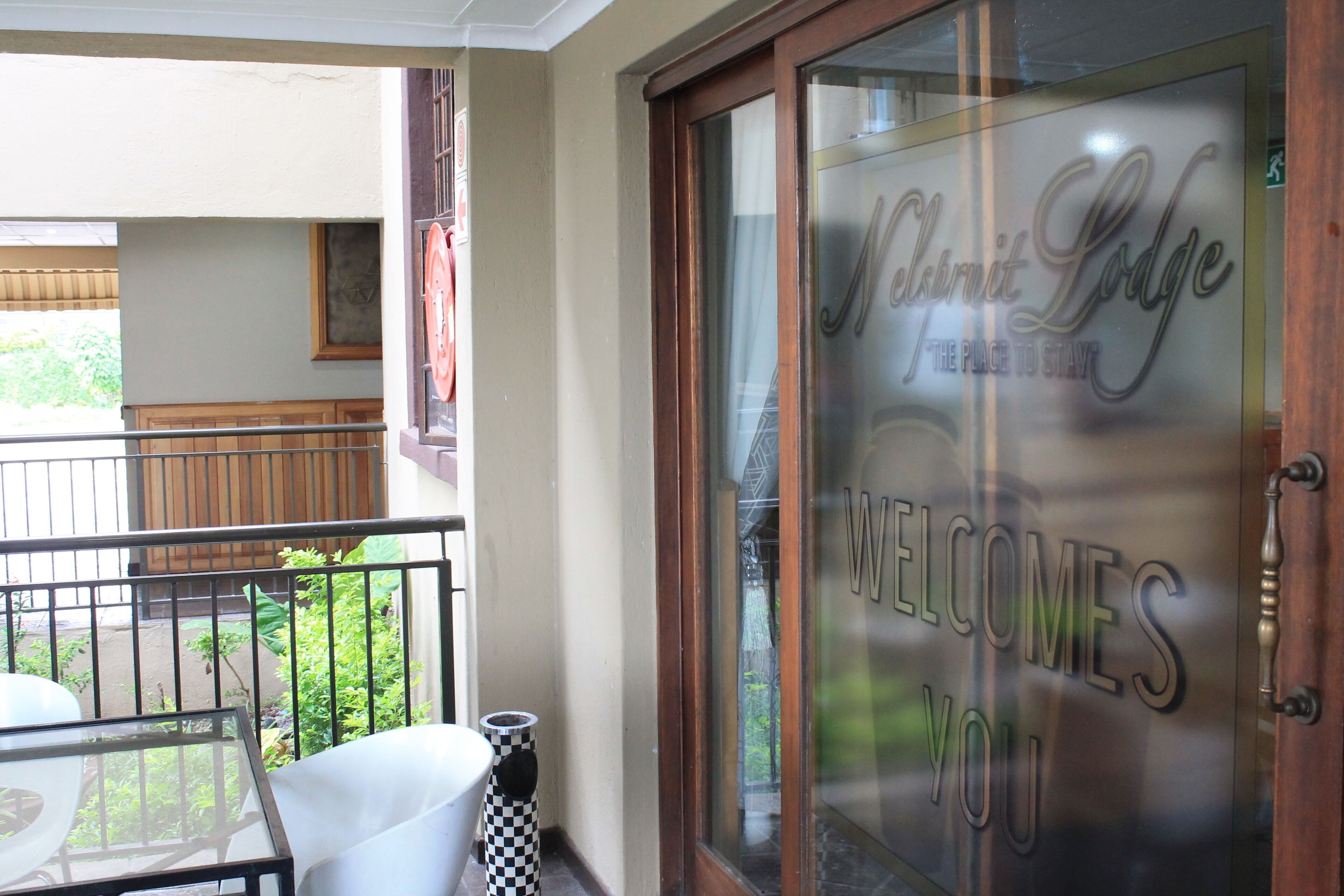 Entrada de un hotel con puerta de vidrio que muestra el letrero "Welcomes You" y "Nelsmit Lodge".