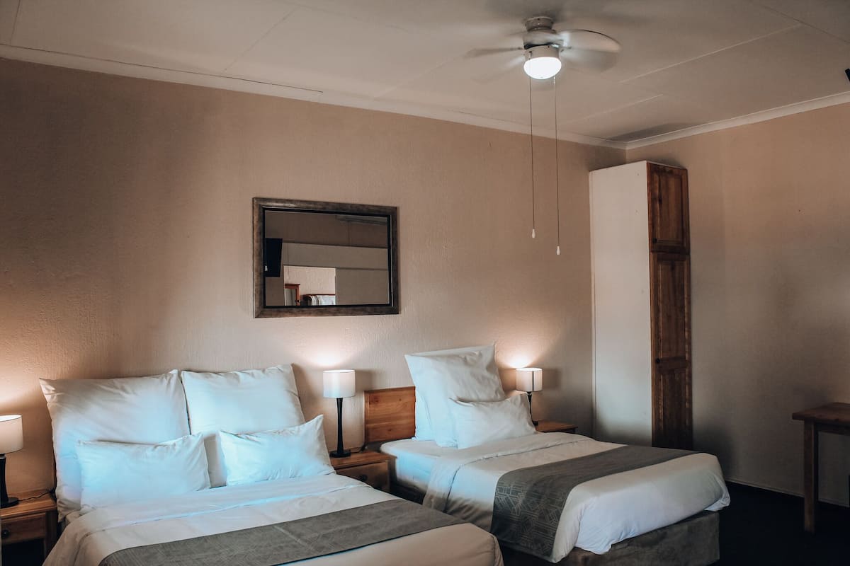 A hotel room with two beds, a ceiling fan, a mirror, and a wardrobe.