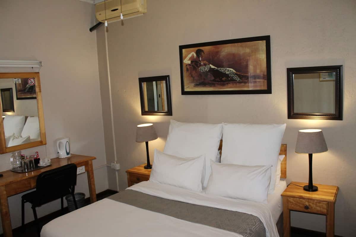 A hotel room with a bed, two bedside tables with lamps, a desk with a chair, a coffee maker, and a painting on the wall.