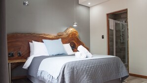 Een moderne slaapkamer met een houten hoofdbord, een grijs gewatteerde spreidek en een douchecabine met glazen wanden.