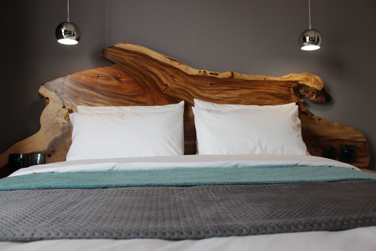 A bed with a wooden headboard, white pillows, and a teal throw blanket.