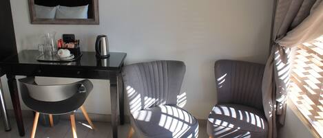 A modern hotel room with a black desk, two grey patterned chairs, a small table, and a mirror on the wall.