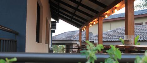 A covered outdoor seating area with wooden tables and chairs, a tiled roof, and a view of a traditional building in the background.