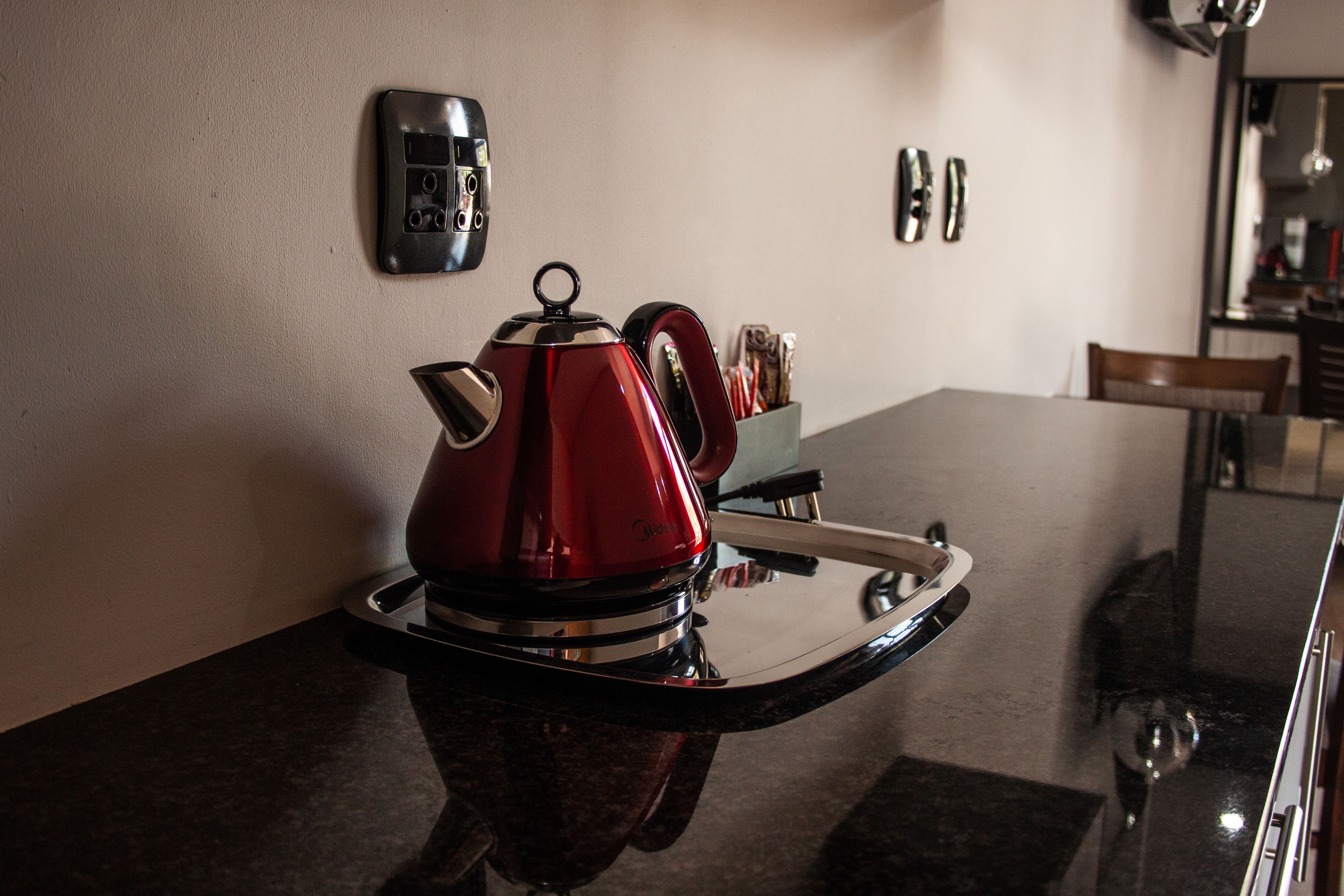 Eine Küche mit einem roten Wasserkocher auf einer Ablage, einer Kaffeemaschine und einem Glas Wasser auf der Arbeitsplatte.