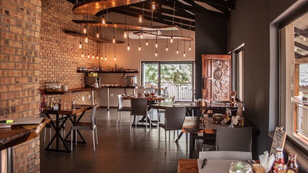 Een restaurant met bakstenen muren, hangende kroonluchters en een mix van houten en metalen meubels.