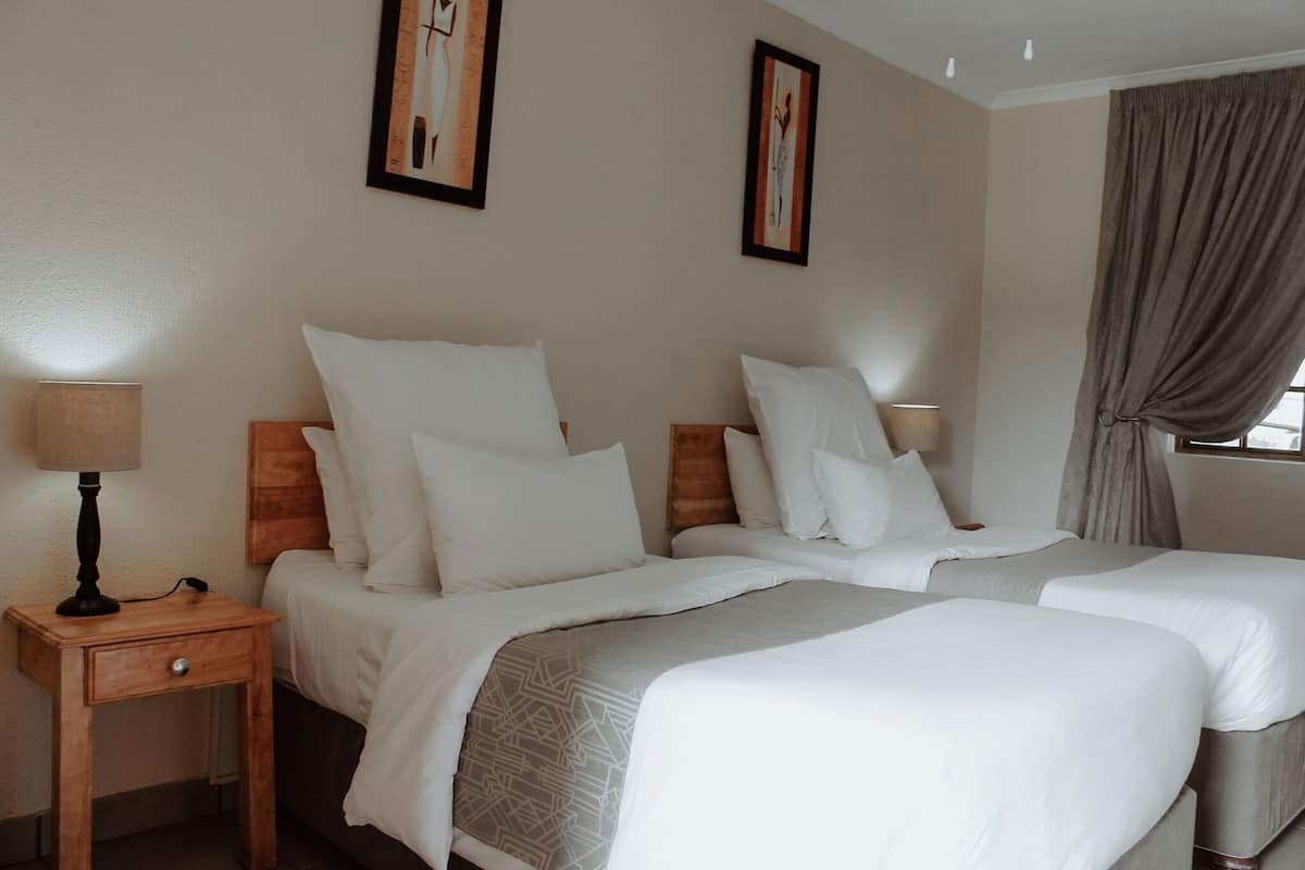 A hotel room with two beds, a nightstand, a lamp, and two framed pictures on the wall.