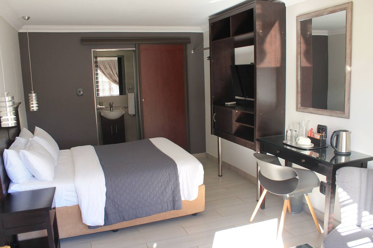 A hotel room with a bed, a desk, a chair, a mirror, and a wardrobe.