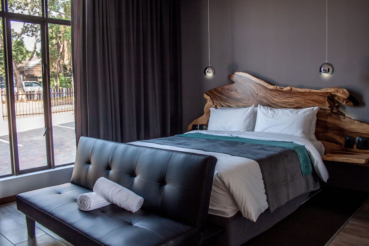 A modern bedroom with a large bed, a leather sofa, and a view of the street outside.