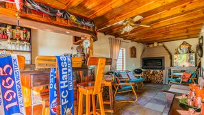 A rustic interior with wooden beams, a bar area, seating with cushions, and a fireplace. - Anchorage Guest House (Plettenberg Bay)