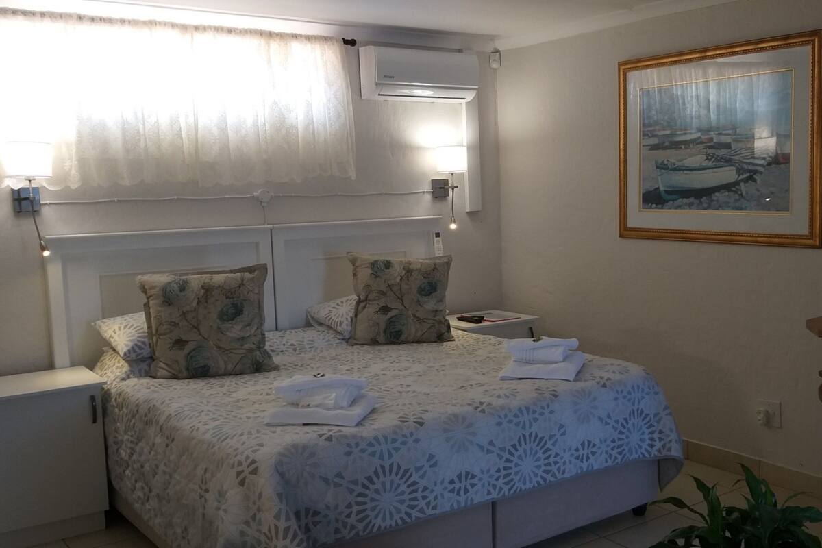 Ein ordentlich gemachtes Bett mit floralen Kissen, ein Nachttisch mit einer Lampe und ein gerahmtes Bild an der Wand.