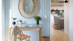 A room with a wooden ceiling, a round mirror, a wicker chair, a small table, and a view into the kitchen. - Coot Club (Stanford)
