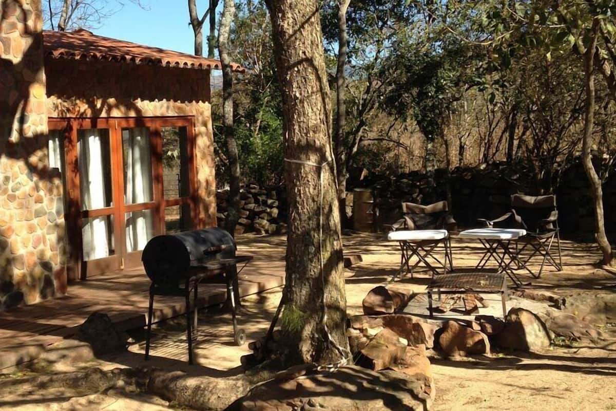 A rustic outdoor area with a stone building, a barbecue grill, and outdoor seating.