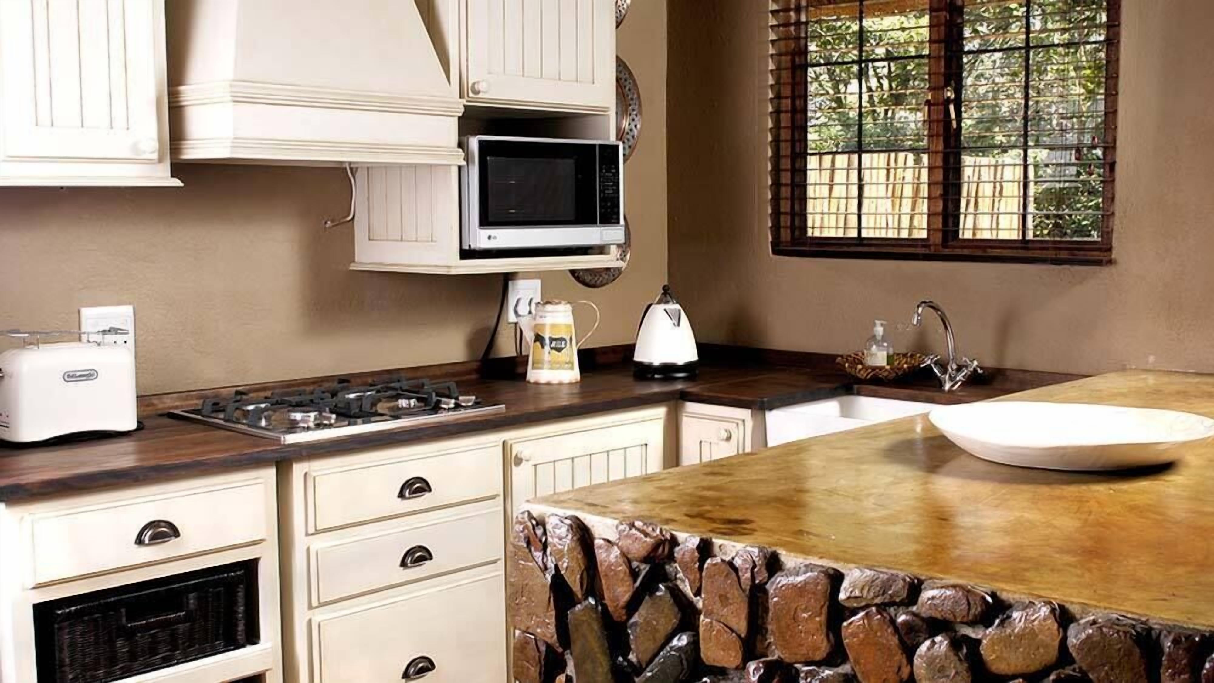 A kitchen with a stone countertop, a sink, a stove, a toaster, a kettle, and cabinets.