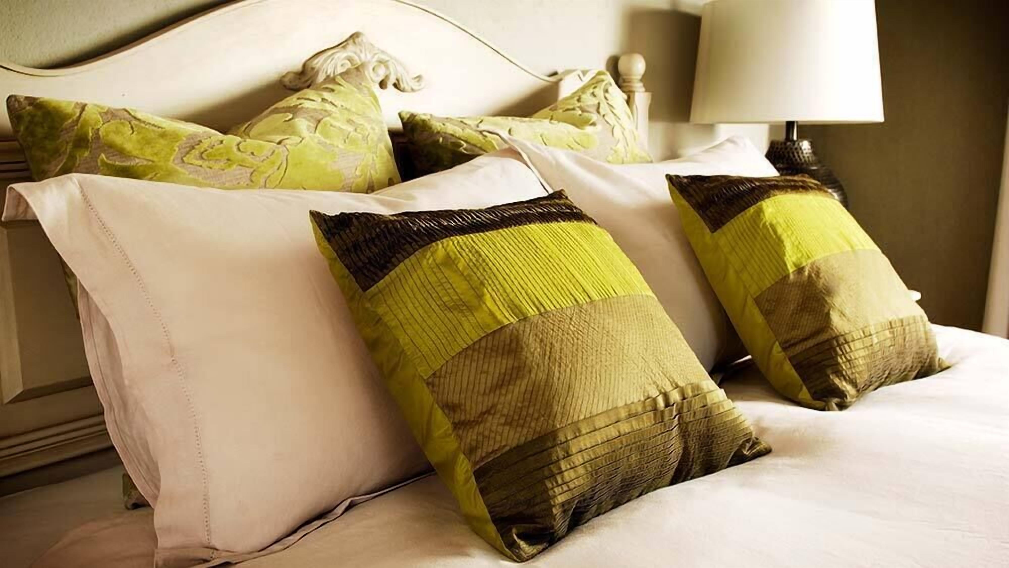 A bed with white bedding and three pillows, one with a green and beige pattern, another with a green and brown pattern, and a plain white pillow.