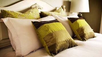 A bed with white bedding and three pillows, one with a green and beige pattern, another with a green and brown pattern, and a plain white pillow.