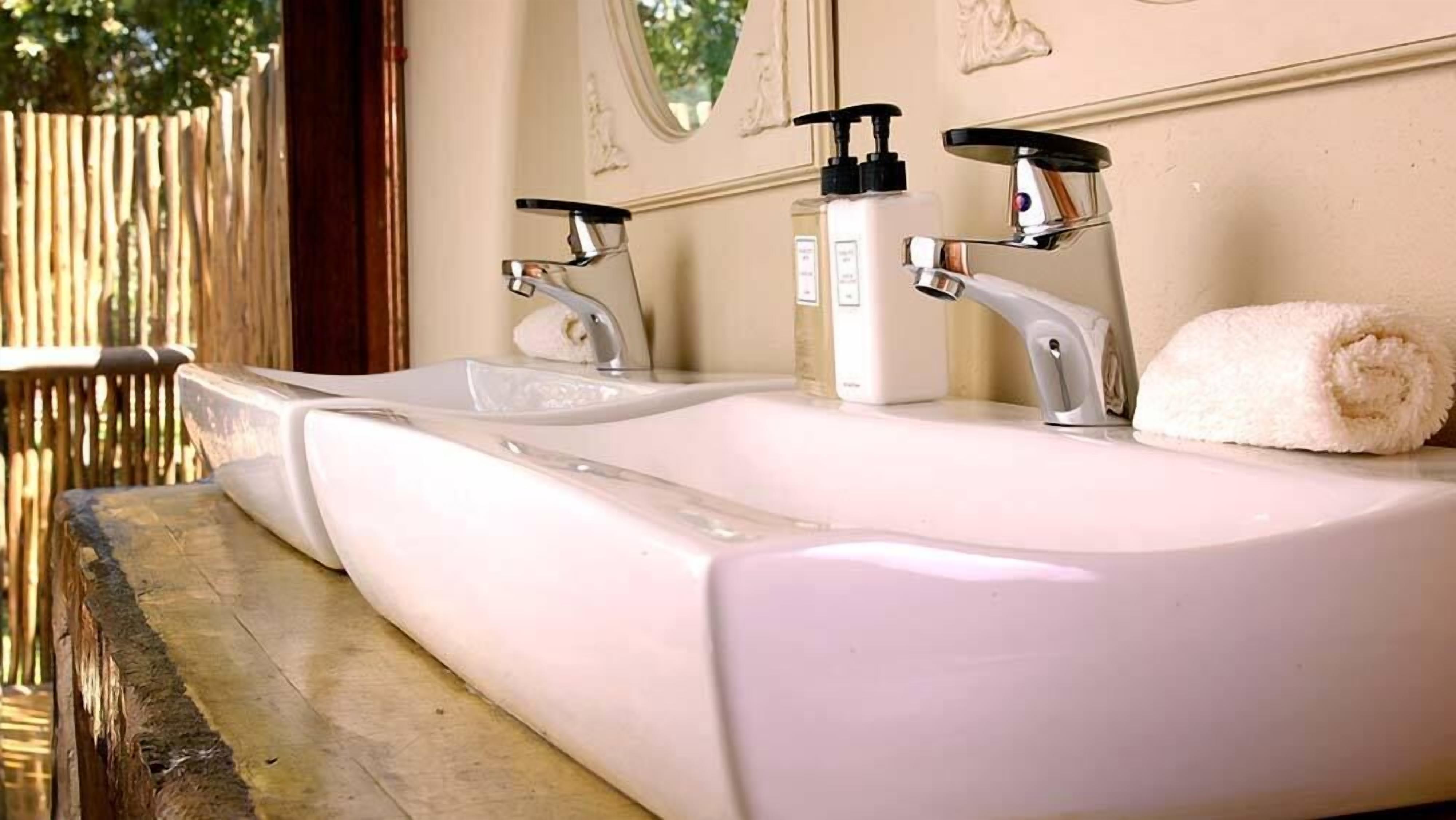 Casa de banho com uma grande pia branca, duas torneiras e uma toalha.