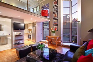 A modern apartment with a kitchen, dining area, and living room. It features a balcony, large windows, and a flat-screen TV. - Cape eazi stayz Old Mutual Apartments (Cape Town)