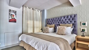 A neatly made bed with a tufted headboard, a bedside table with a lamp, and a wall-mounted artwork. - Cape eazi stayz Old Mutual Apartments (Cape Town)