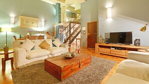 A living room with a sofa, coffee table, TV, and a staircase leading to an upper level. - Cape eazi stayz Old Mutual Apartments (Cape Town)