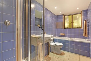 A bathroom with blue tiles, a glass shower enclosure, a sink, a toilet, and a bathtub.