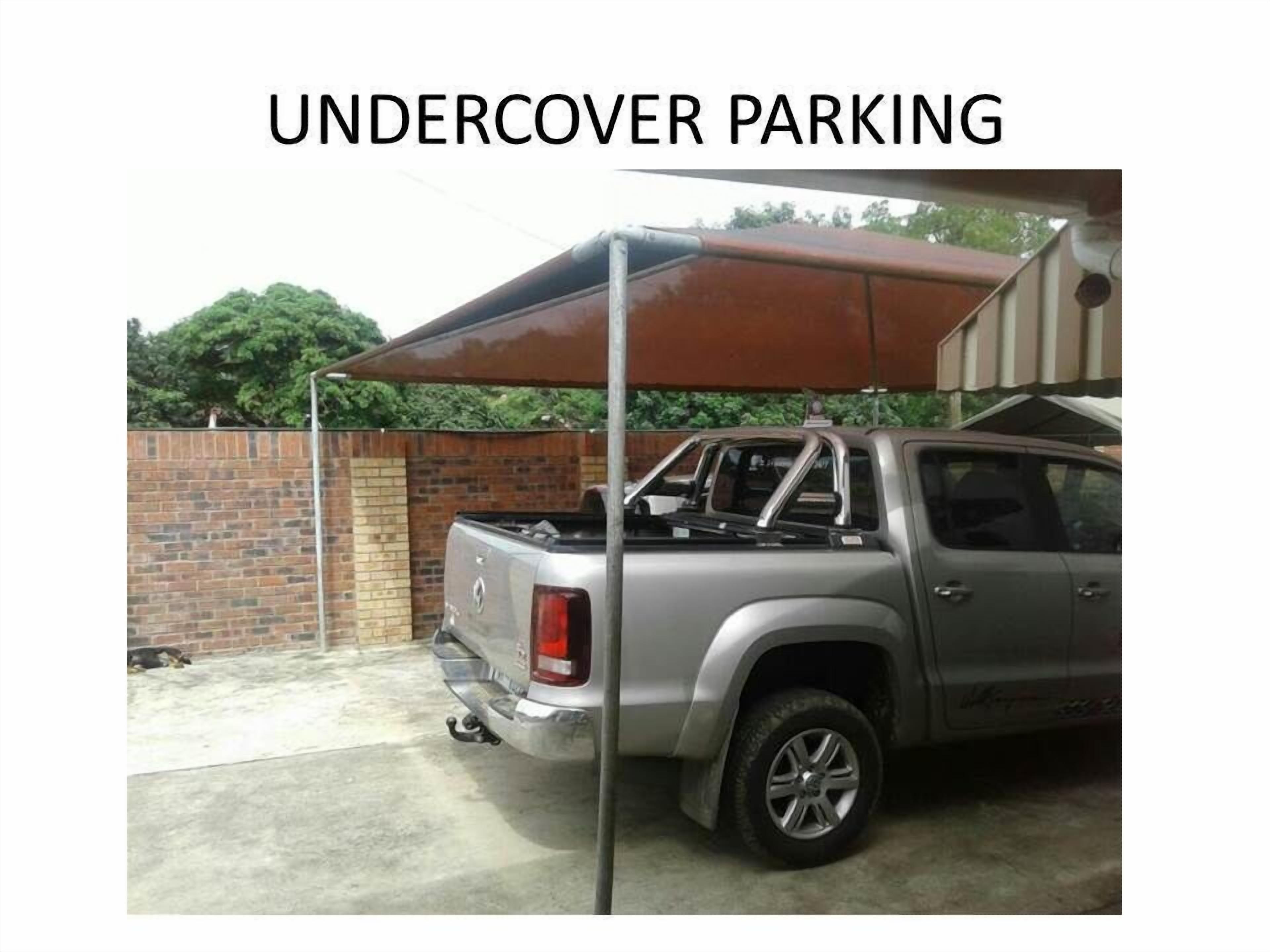 A silver pickup truck parked under a covered area with a brick wall and greenery in the background.