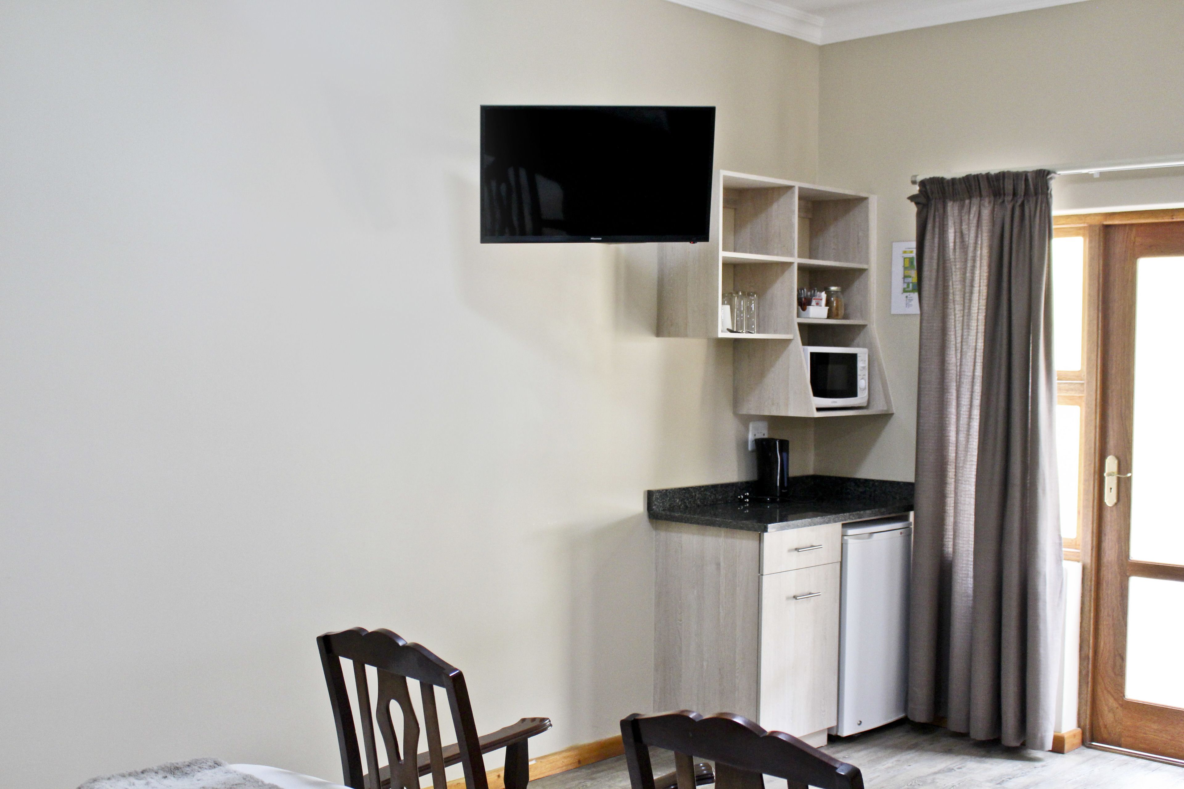 A compact kitchen with a microwave, a coffee machine, and a flat-screen TV mounted on the wall.