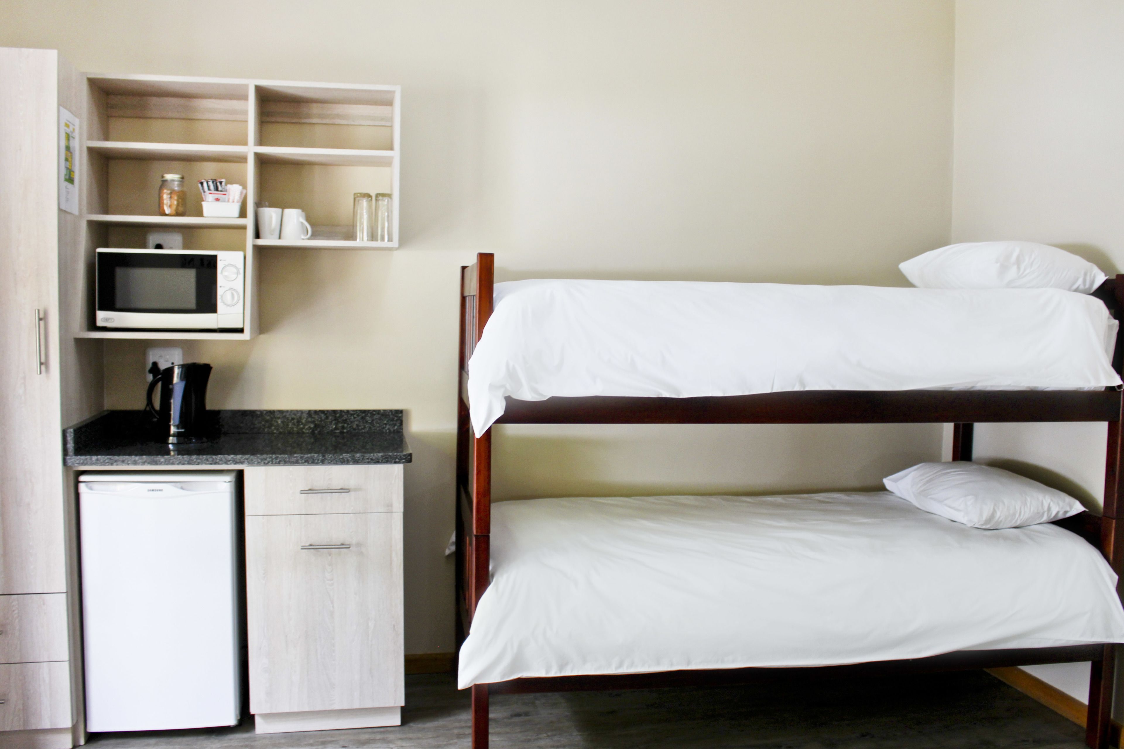 A bunk bed with white bedding, a microwave, and a small kitchenette with a refrigerator.